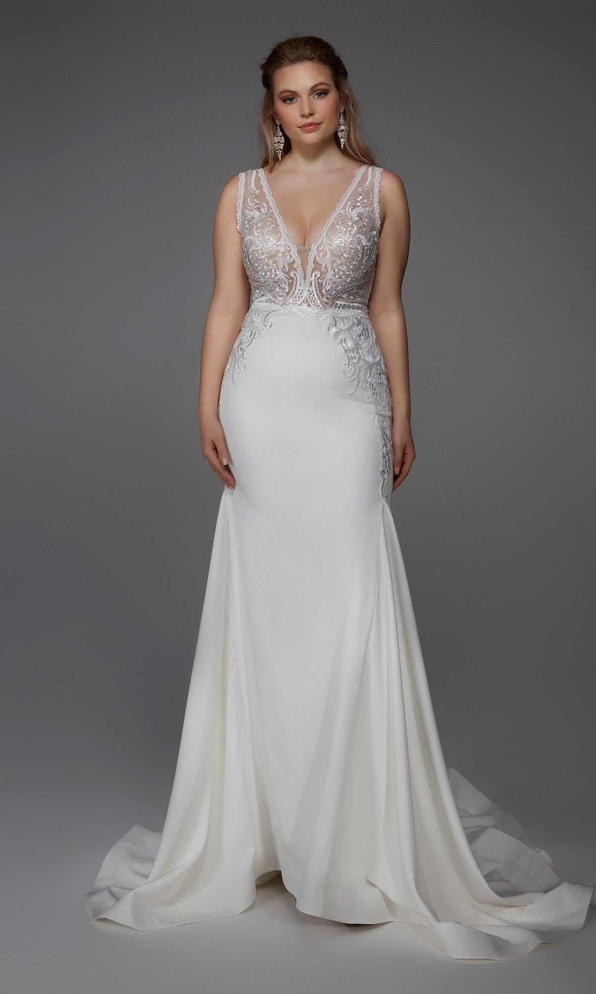 A woman in the Long White Dress: Alyce 7016, featuring an ivory sleeveless gown with a fitted embroidered bodice and flowing skirt, stands against a plain gray background.